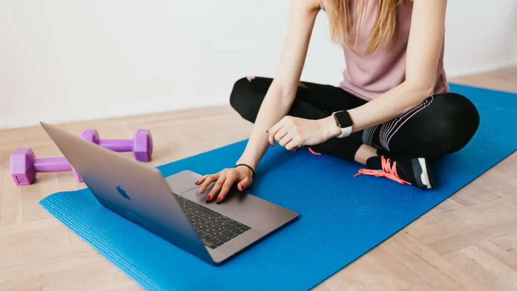 Mujer entrenando en casa sobre la esterilla, siguiendo su plan en el portátil