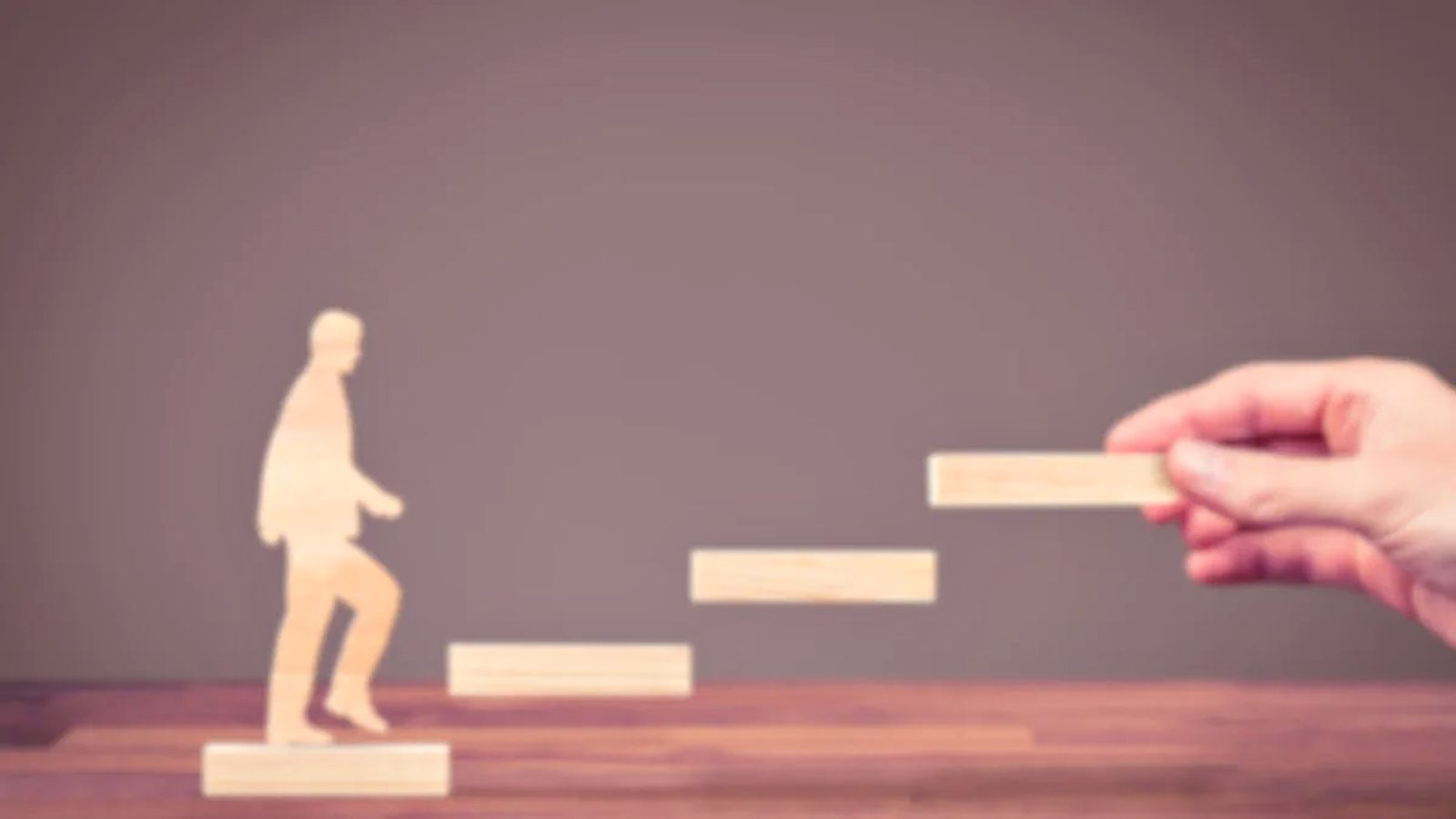 Figura de madera subiendo una escalera de peldaños que alguien va colocando