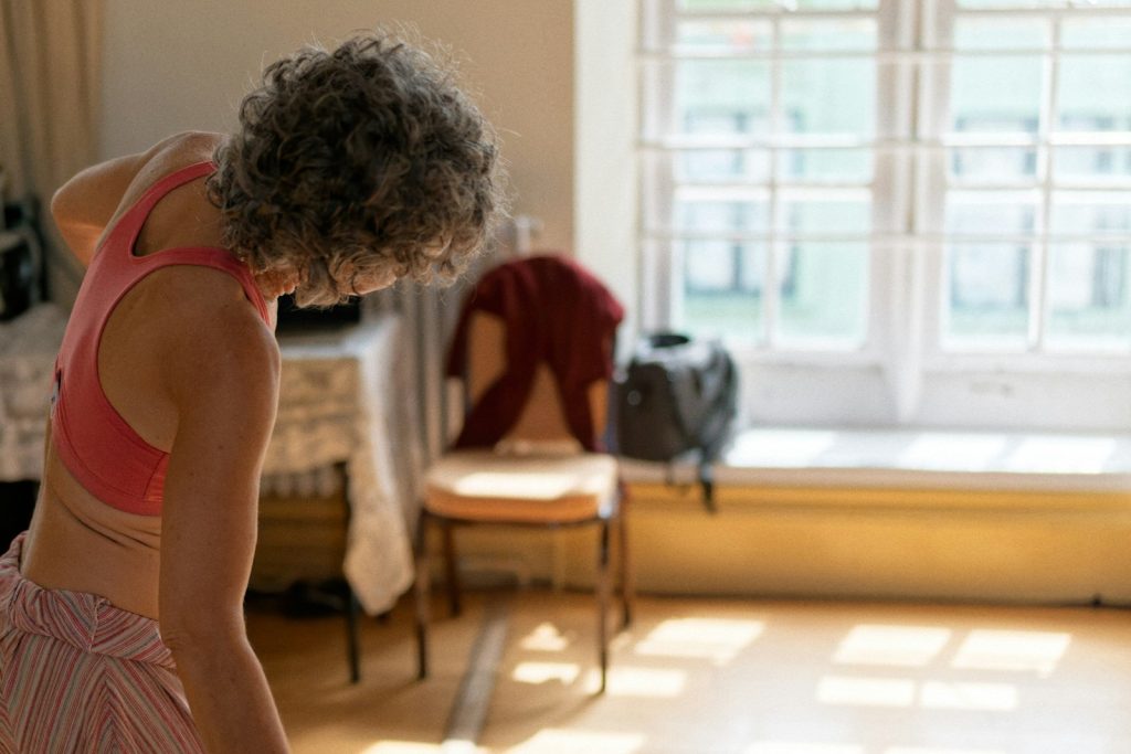 Mujer madura estirando con calma en su salón con luz natural